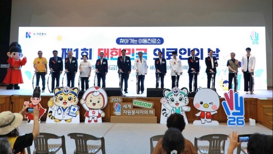 ‘제1회 대한민국 의료인의 날’ 기념식 무대에 참석자들이 나란히 서 있고 무대 앞에 봉사 캐릭터 입간판이 놓인 모습